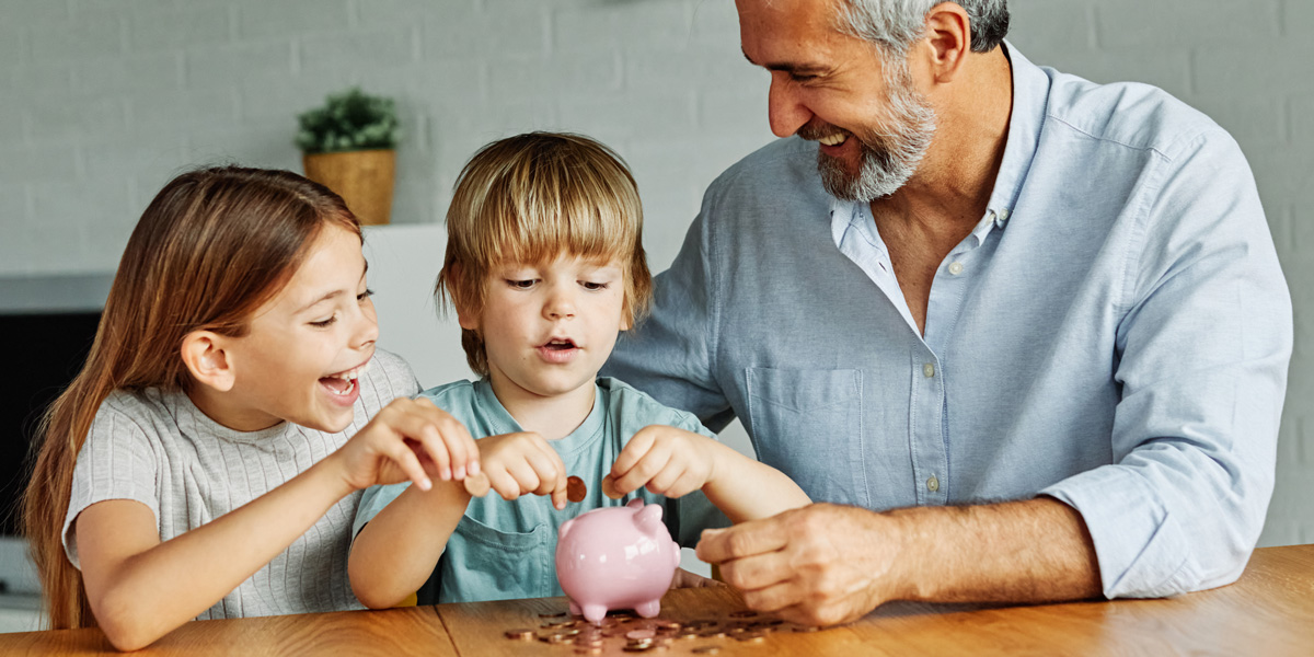 Grandfather with two grandchildren adding coins to a piggy bank