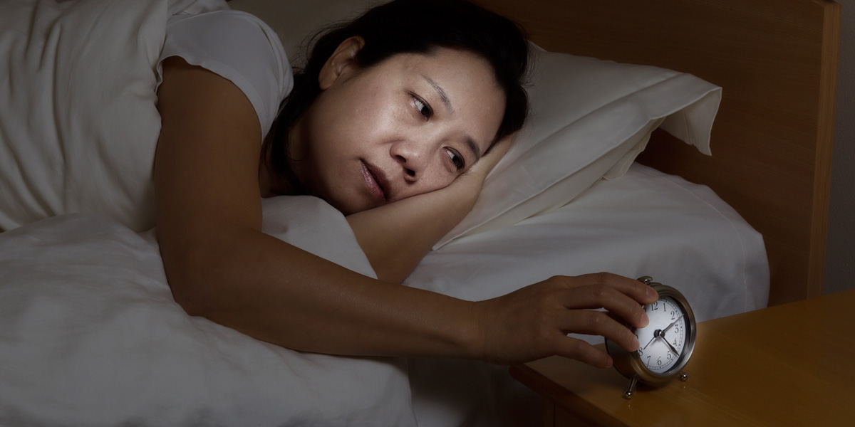 Woman in bed looking at an alarm clock