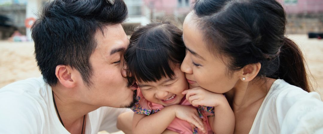 Two parents kissing a young girl