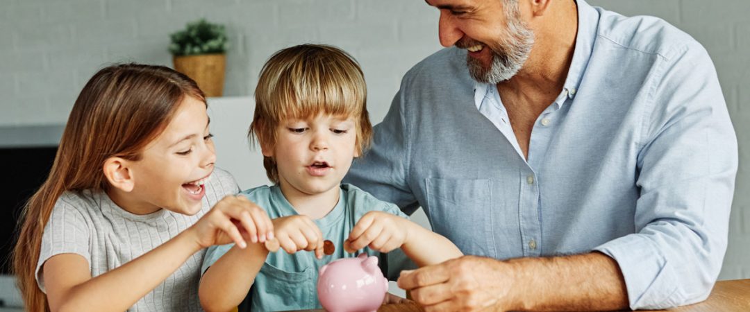Grandfather with two grandchildren adding coins to a piggy bank
