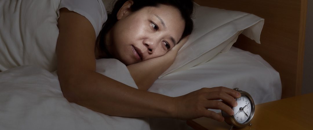 Woman in bed looking at an alarm clock