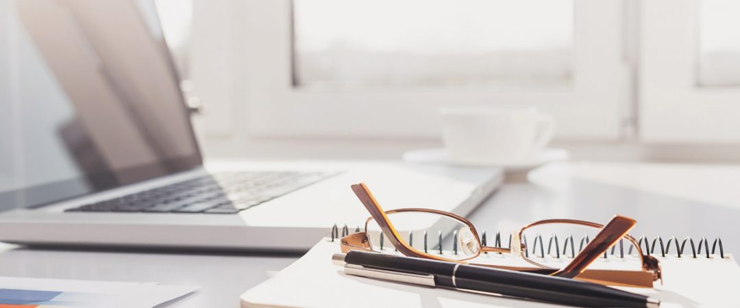 Desk with laptop, glasses, pen and notepad